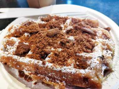Tek kullanımlık kağıt tabakta servis edilen taze pişmiş Belçika waffle 'ının ağız sulandırıcı görüntüsü. Bu popüler sokak yemekleri tatlı kurabiye parçaları ve krema şekeri ile kaplıdır. Hızlı bir atıştırmalık ya da kahvaltı düşkünlüğü için mükemmeldir..