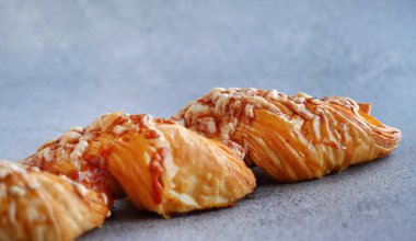 Erimiş peynir ve baharatlı sosla kaplanmış lezzetli bir poğaçanın yakın görüntüsü. Fırının altın-kahverengimsi yumuşacık dokusu, en az gri beton arka planıyla çok güzel zıtlaşır. Kahvaltı ya da atıştırmalık için mükemmeldir.