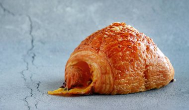 Sıcak, yeni pişmiş jambonlu ve peynirli kruvasan yakın çekim. Görüntü, altın-kahverengi puf puf böreği katmanlarını ve en az gri beton dokunun üzerine kurulmuş lezzetli erimiş peyniri ön plana çıkarıyor. Fırın ve B için mükemmel.