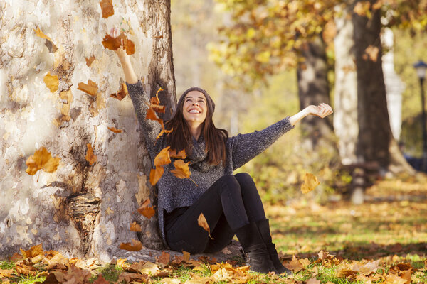 Женщина капает листья в осеннем парке
