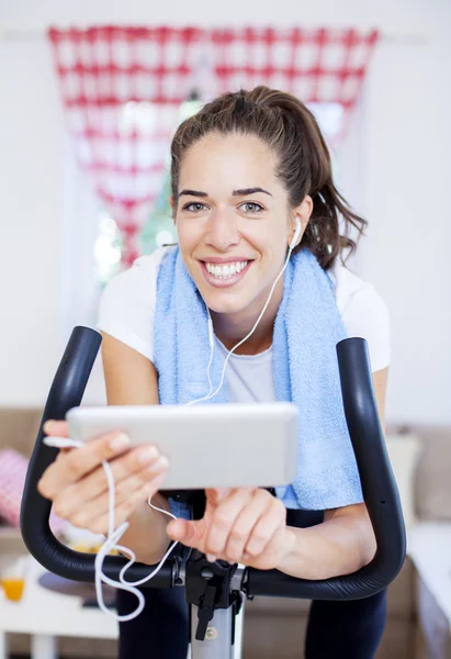 Woman training on exercise bike using tablet — Stock Photo, Image