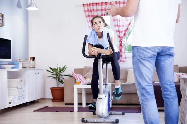 Kobieta, szkolenia na rower treningowy w pokoju — Zdjęcie stockowe