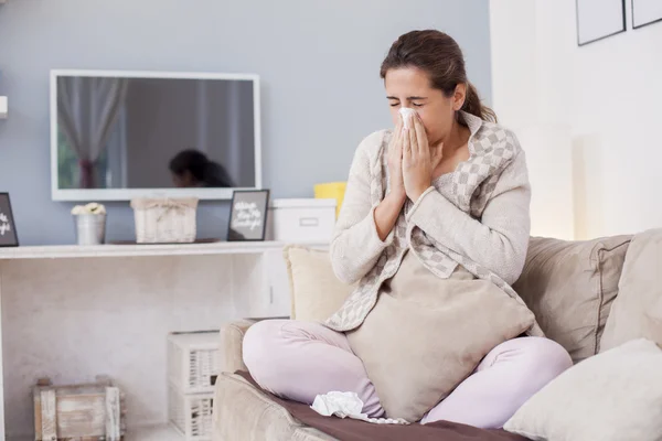 Sick woman blowing nose on sofa — Stok Foto