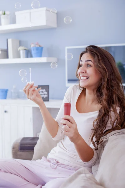 Hermosa mujer soplando burbujas en su sala de estar, divirtiéndose. Profundidad superficial del campo — Foto de Stock