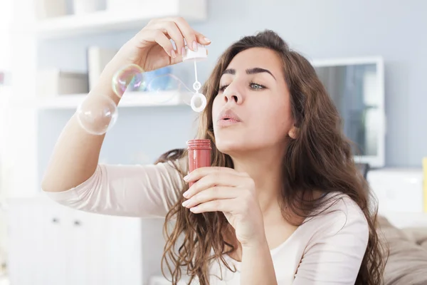 Belle femme soufflant des bulles dans son salon, s'amusant. Profondeur de champ faible — Photo