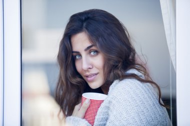 Genç ve güzel bir kadın kahve içiyor ve pencereden dışarı bakıyor.