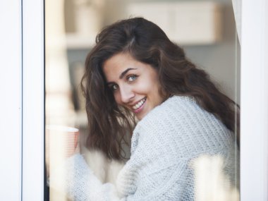 Genç ve güzel bir kadın kahve içiyor ve pencereden dışarı bakıyor.