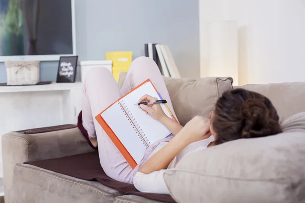 Mooie jonge vrouw zit op haar gezellige bed en het maken van notities aan haar dagboek, ondiepe scherptediepte geplaatst — Stockfoto