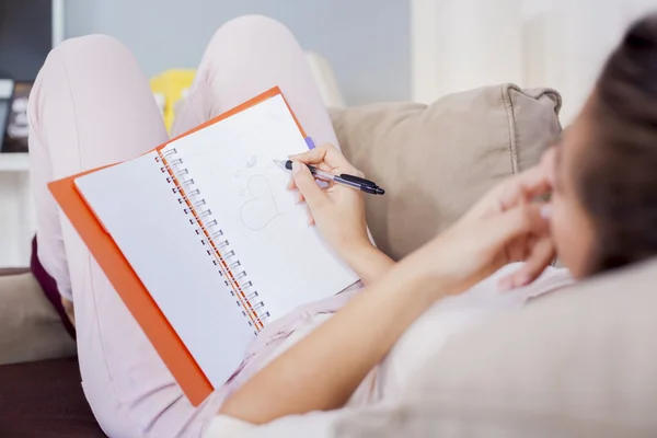 Jolie jeune femme assise sur son lit douillet et prenant des notes à son journal intime, peu profonde de limé — Photo