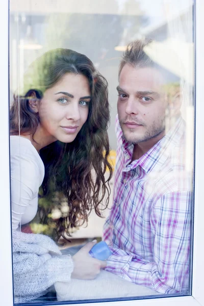 Un beau jeune couple debout à la fenêtre à la maison . — Photo