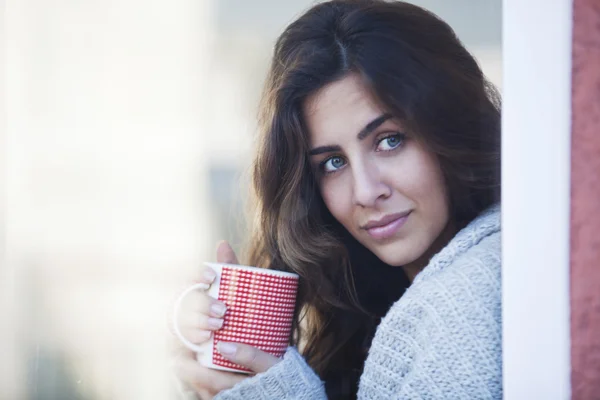 Wanita muda cantik minum kopi dan melihat ke luar jendela — Stok Foto