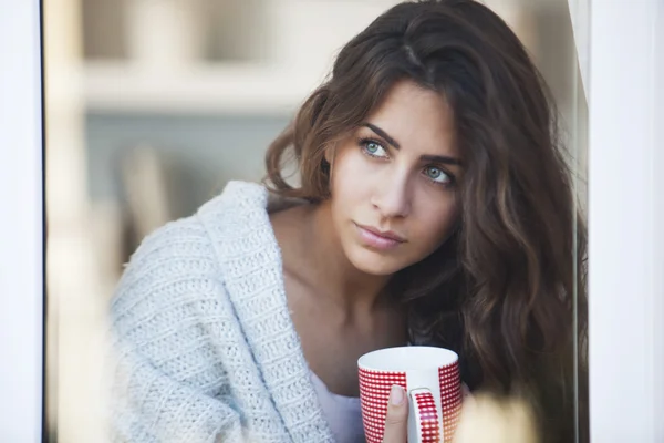 Junge schöne Frau trinkt Kaffee und schaut aus dem Fenster — Stockfoto