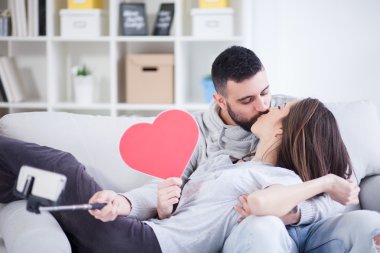 Fotoğrafta akıllı telefon ile selfie çubuğa mutlu genç güzel bir çift. Genç çift oturma odasında eğleniyor