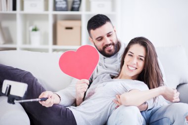 Fotoğrafta akıllı telefon ile selfie çubuğa mutlu genç güzel bir çift. Genç çift oturma odasında eğleniyor