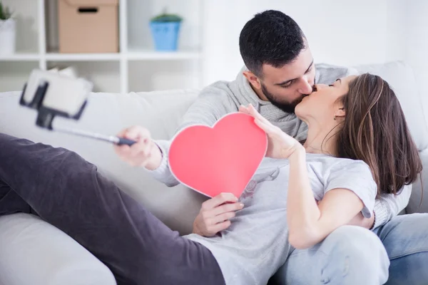 Joyeux jeune beau couple prenant des photos avec téléphone intelligent sur selfie stick. Jeune couple s'amusant dans le salon — Photo