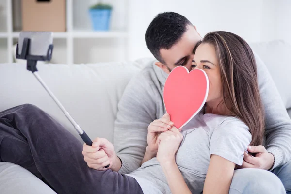 Joyeux jeune beau couple prenant des photos avec téléphone intelligent sur selfie stick. Jeune couple s'amusant dans le salon — Photo