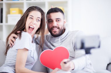 Fotoğrafta akıllı telefon ile selfie çubuğa mutlu genç güzel bir çift. Genç çift oturma odasında eğleniyor