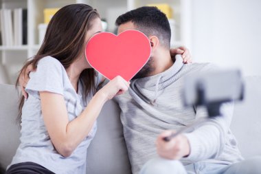 Fotoğrafta akıllı telefon ile selfie çubuğa mutlu genç güzel bir çift. Genç çift oturma odasında eğleniyor