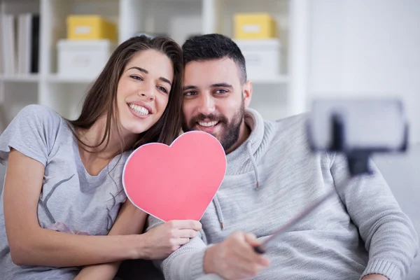 Glückliches junges schönes Paar beim Fotografieren mit Smartphone auf Selfie-Stick. junges Paar hat Spaß im Wohnzimmer — Stockfoto