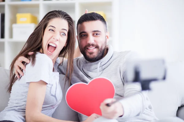 Joyeux jeune beau couple prenant des photos avec téléphone intelligent sur selfie stick. Jeune couple s'amusant dans le salon — Photo