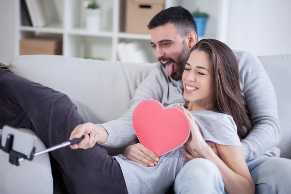 행복 한 젊은 아름 다운 커플 selfie 막대기에 스마트 폰으로 사진을 복용. 젊은 부부는 거실에 있는 재미 — 스톡 사진