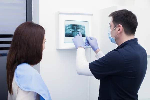 Mieshammaslääkäri näyttää röntgenkuvaa potilaalleen hammashoitolassa. — kuvapankkivalokuva