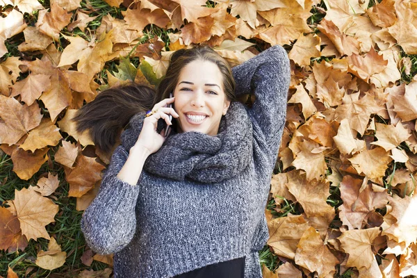 Portrait d'une automnale allongée sur des feuilles et souriante parlant au téléphone — Photo