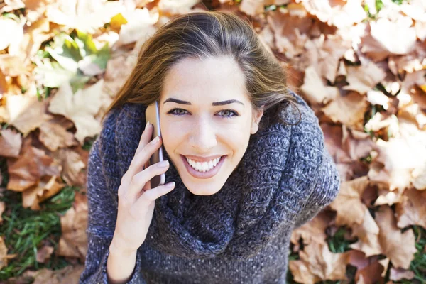 Портрет осенней женщины, лежащей над листьями и улыбающейся разговаривающей по телефону — стоковое фото
