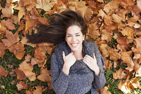 Retrato de uma mulher de outono deitada sobre folhas e sorrindo — Fotografia de Stock