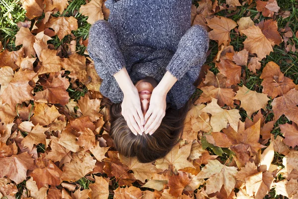 Retrato de una mujer de otoño acostada sobre hojas y sonriente —  Fotos de Stock