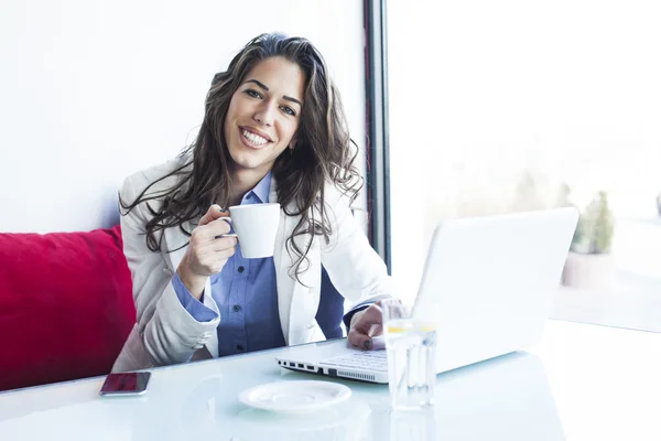 Молода ділова жінка сидить у каві біля вікна, працюючи на ноутбуці, маючи каву — стокове фото
