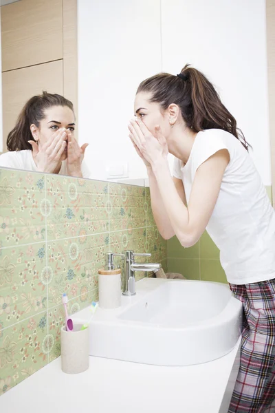 Donna spruzzando faccia con acqua sopra lavello del bagno — Foto Stock