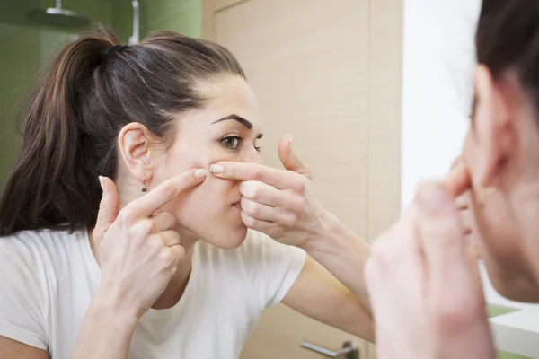 Mujer joven aprieta su acné delante del espejo. Problemas de la piel, colmena de mujer — Foto de Stock