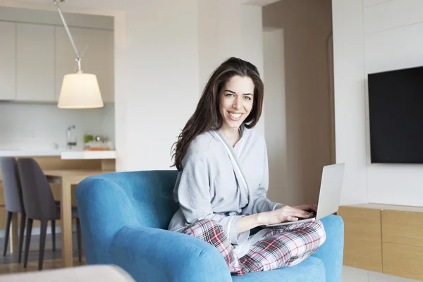 Mujer sentada en un sofá en el salón. Escena de la mañana, mujer sonriendo trabajando en el portátil —  Fotos de Stock