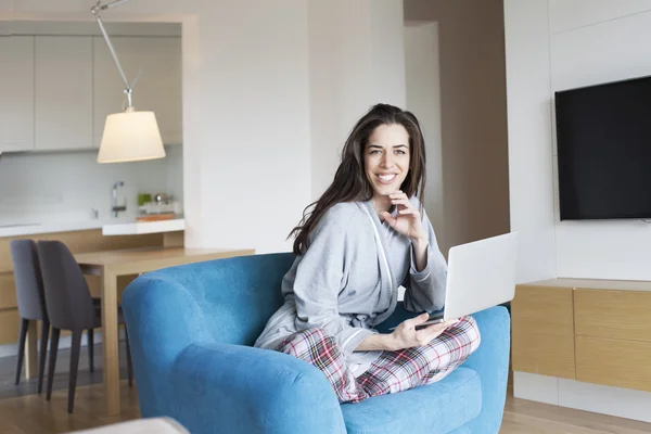 Donna seduta sul divano in soggiorno. Scena mattutina, donna sorridente che lavora su laptop — Foto Stock