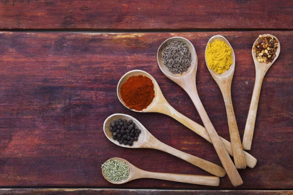 Cucharas de madera llenas de hierbas aromáticas y especias en una tabla de cortar de madera — Foto de Stock