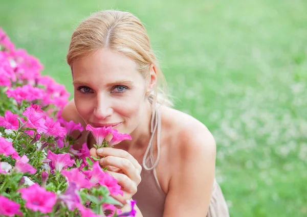 Güzel sarışın genç kadın bir bahçede çiçek kokuyor — Stok fotoğraf