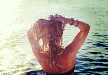 Harika bir genç kadın denize izliyor ve elleri üzerinde gündoğumu yükselterek bir arka yan görünüm