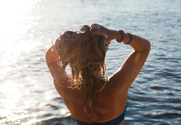 Uma visão lateral traseira em uma jovem mulher maravilhosa assistindo ao mar e levantando as mãos no nascer do sol — Fotografia de Stock