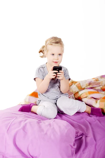 Cute little blonde girl under the pillow laughing and lying on the bed with purple linen — Stock Photo, Image