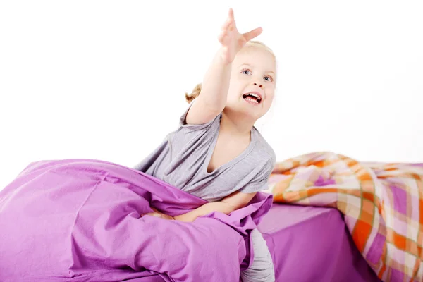 Aranyos szőke kislány a párna, nevetett, és az ágyon lila vászon — Stock Fotó