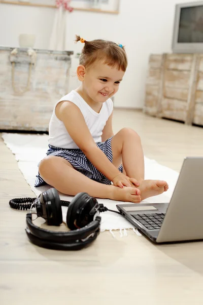 Lilla flickan ler och spelar på den bärbara datorn i vardagsrummet — Stockfoto