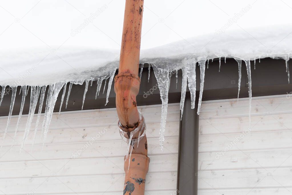Row of icicles on the snow covered roof with a busted pipe