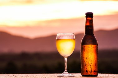 Şişe ve bardak günbatımı üzerinde hafif bira