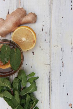 Bir fincan limonlu çay, zencefil kökü ve ahşap bir masada nane yaprağı. Bir bardak dolusu limon çayı. Koyu ahşap bir masada bir fincan. İçinde limon dilimi ve organik zencefil kökü olan güzel bir fincan. Boşluğu kopyala. 
