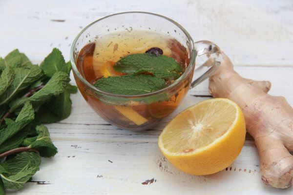 чашку чая с лимоном, имбирным корнем и мятными листьями на деревянном столе. Стакан лимонного чая. Чашка на тёмном деревянном столе. Прекрасная чашка с вырезанным лимоном и органическим корнем имбиря. Копирование пространства. 