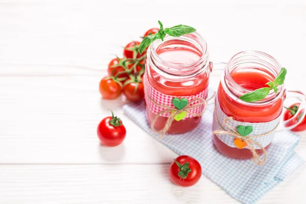 Tomatensap en verse tomaten op een witte houten achtergrond — Stockfoto