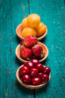Taze kiraz, çilek ve kayısı yeşil ahşap masa üzerinde bir kasede.