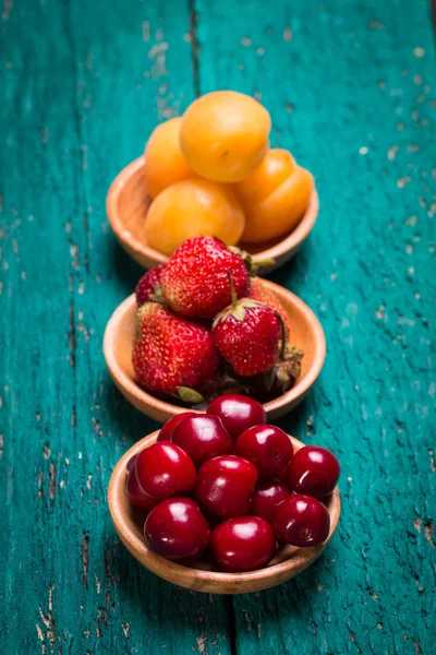 Taze kiraz, çilek ve kayısı yeşil ahşap masa üzerinde bir kasede.