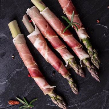 Parma jambonu bir kesme tahtası üzerinde sarılı taze organik kuşkonmaz 